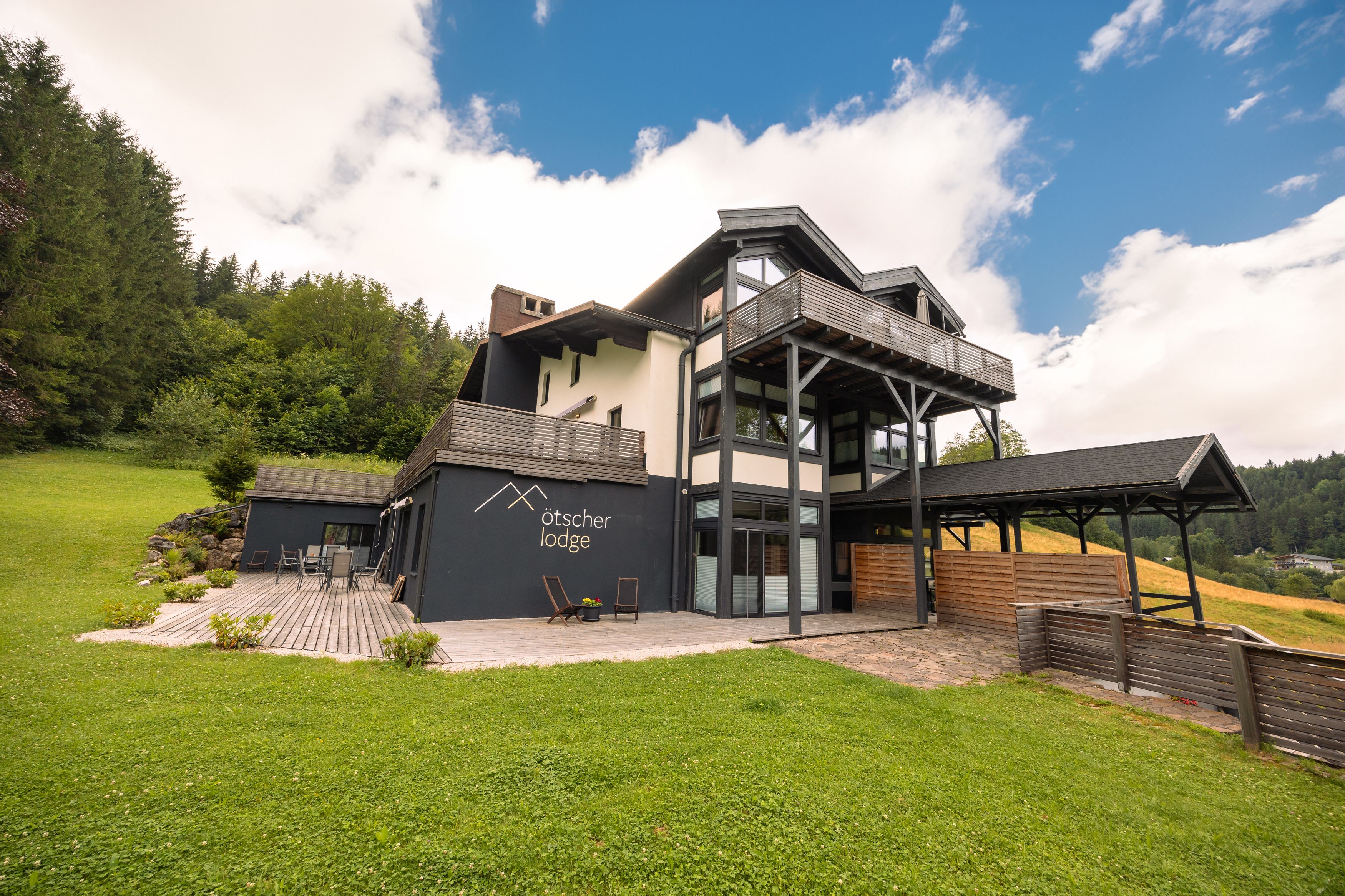 Ötscher Lodge in einer grünen, bewaldeten Umgebung mit blauem Himmel.