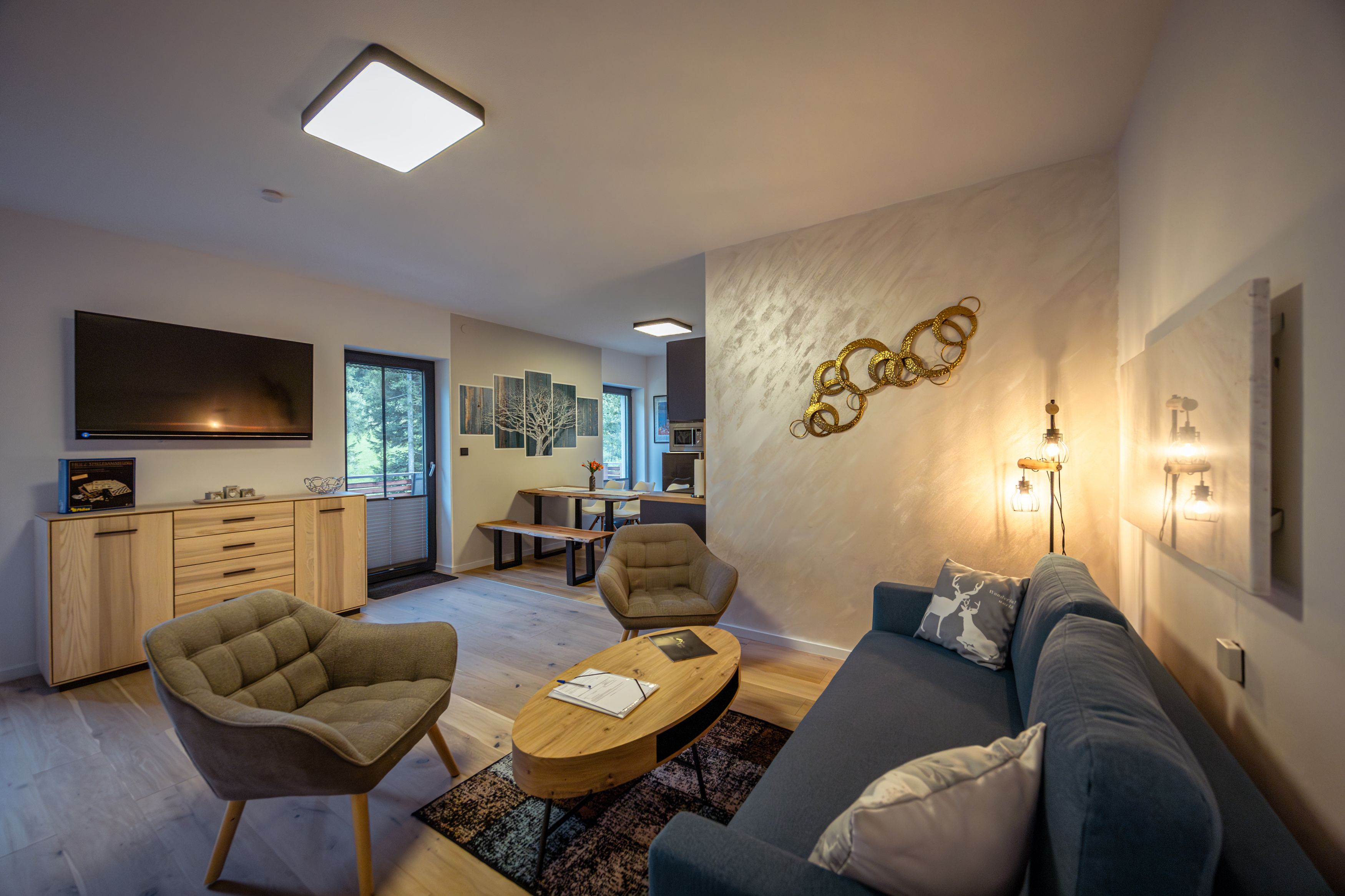 Modern eingerichtetes Wohnzimmer mit Sofa, Sesseln, TV und Esstisch.
