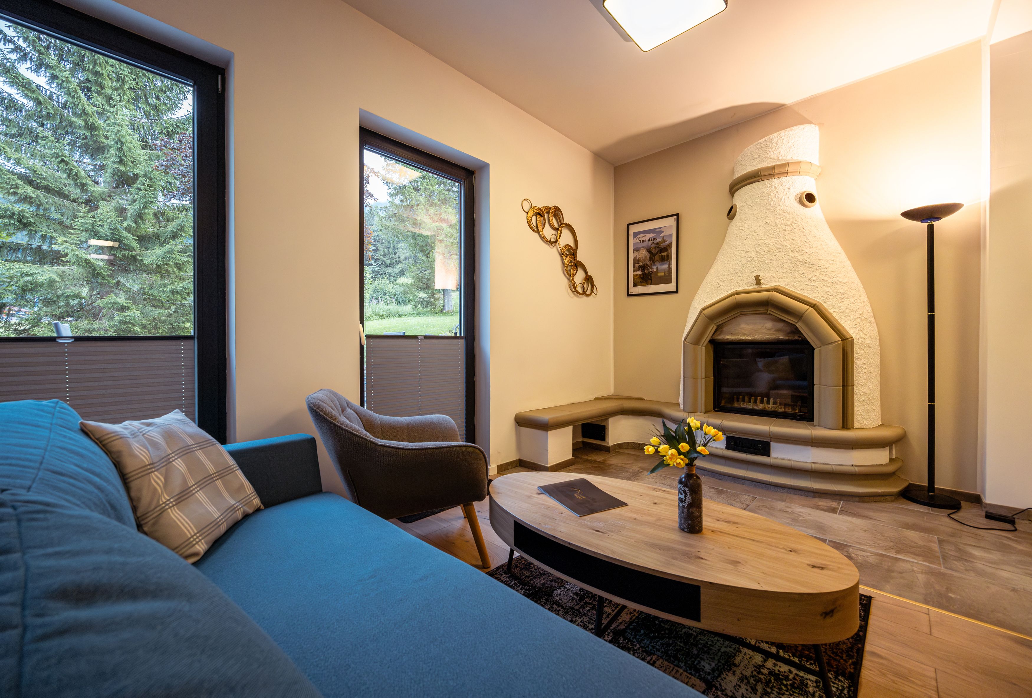 Gemütliches Wohnzimmer mit Kamin, Sofa, Sessel und Couchtisch. Große Fenster mit Blick ins Grüne.