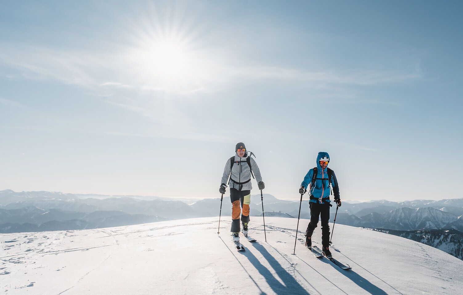 Zwei Skitourengeher genießen die frische Winterluft und die atemberaubende Aussicht auf die schneebedeckten Berge. Die glitzernde Schneedecke reflektiert das Sonnenlicht und schafft eine magische Atmosphäre, die zum Erkunden einlädt.