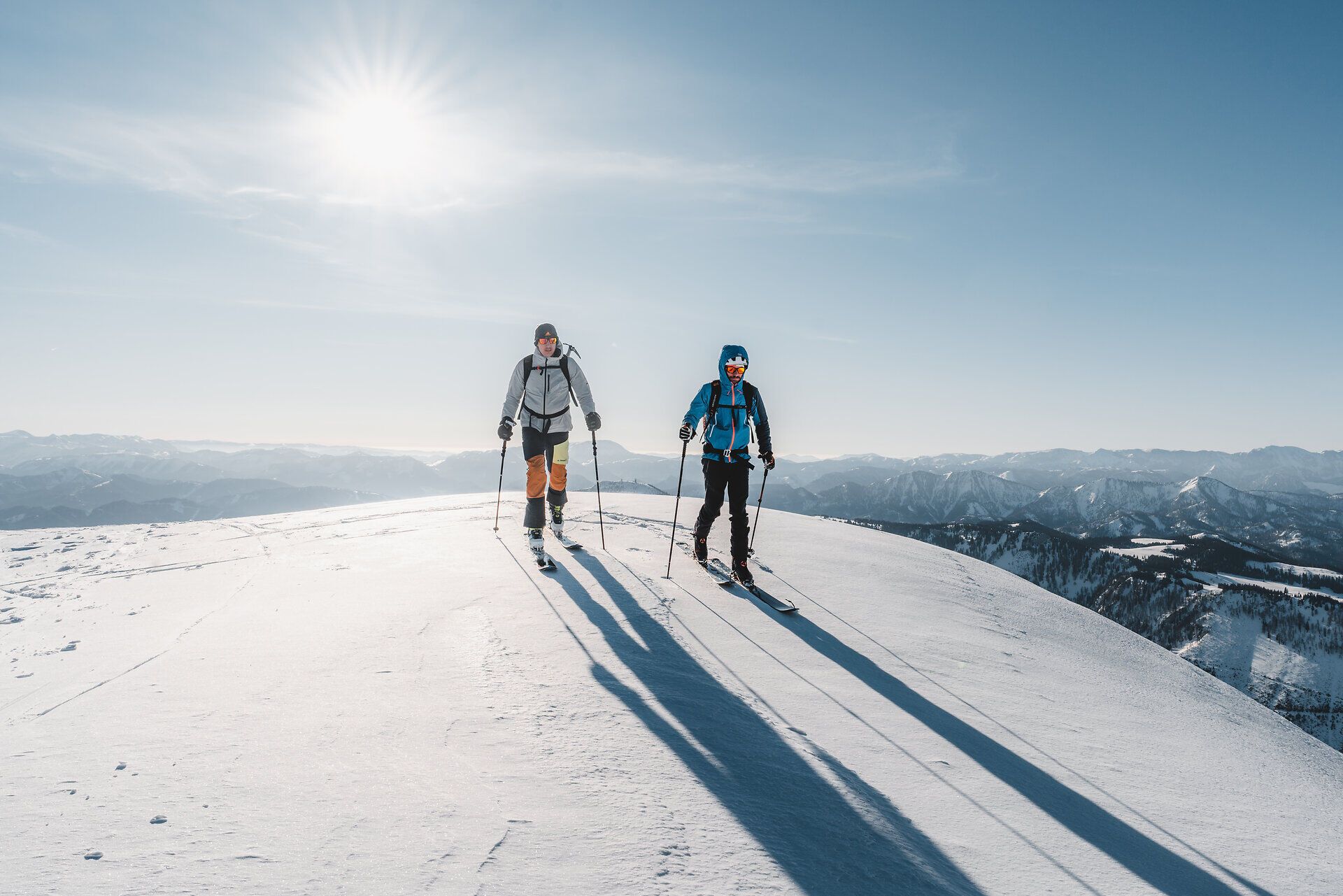 Zwei Skitourengeher genießen die frische Winterluft und die atemberaubende Aussicht auf die schneebedeckten Berge. Die glitzernde Schneedecke reflektiert das Sonnenlicht und schafft eine magische Atmosphäre, die zum Erkunden einlädt.